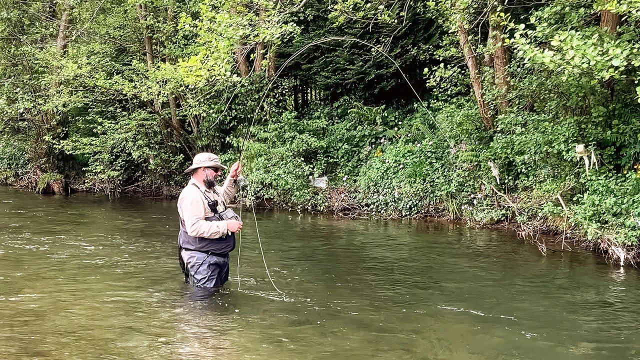 Pescador a mosca tensando la línea con la caña doblada en un río, ejemplo real de control y precisión en el lanzado