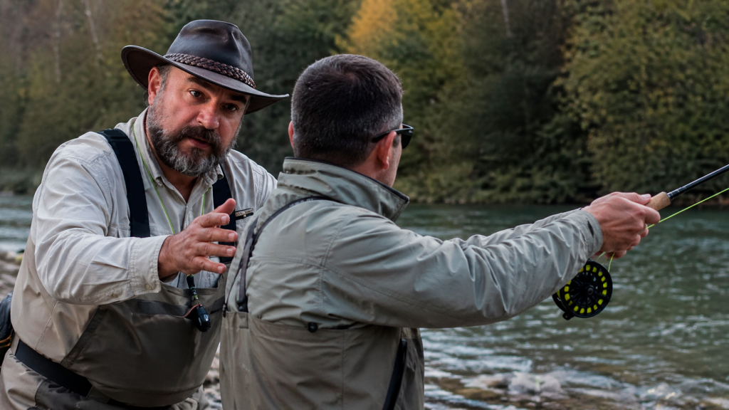 Instructor de pesca con mosca corrigiendo a un alumno durante un curso en el río